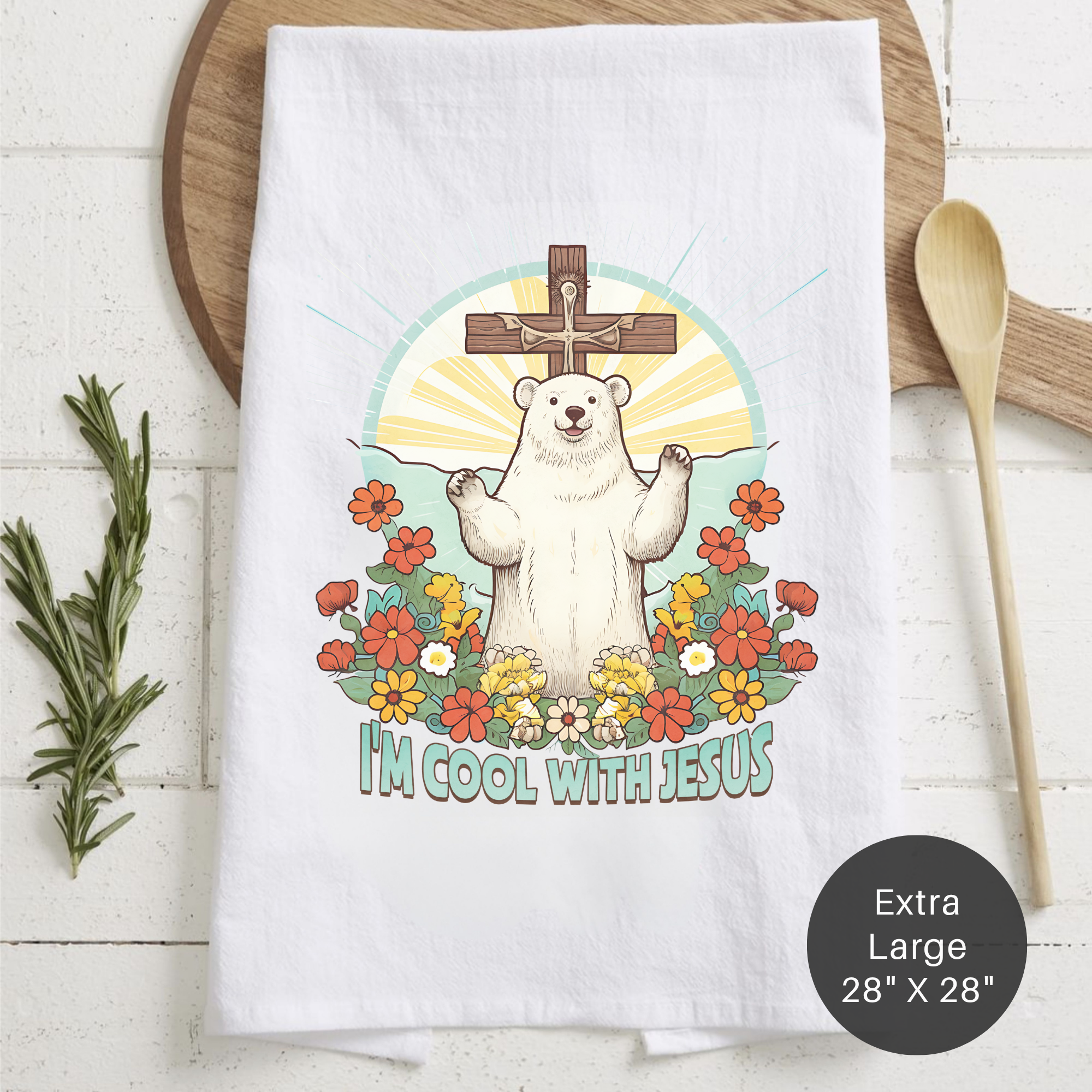 White tea towel with a bear in front of a cross and flowers, text 'I'm cool with Jesus', on a wooden surface.