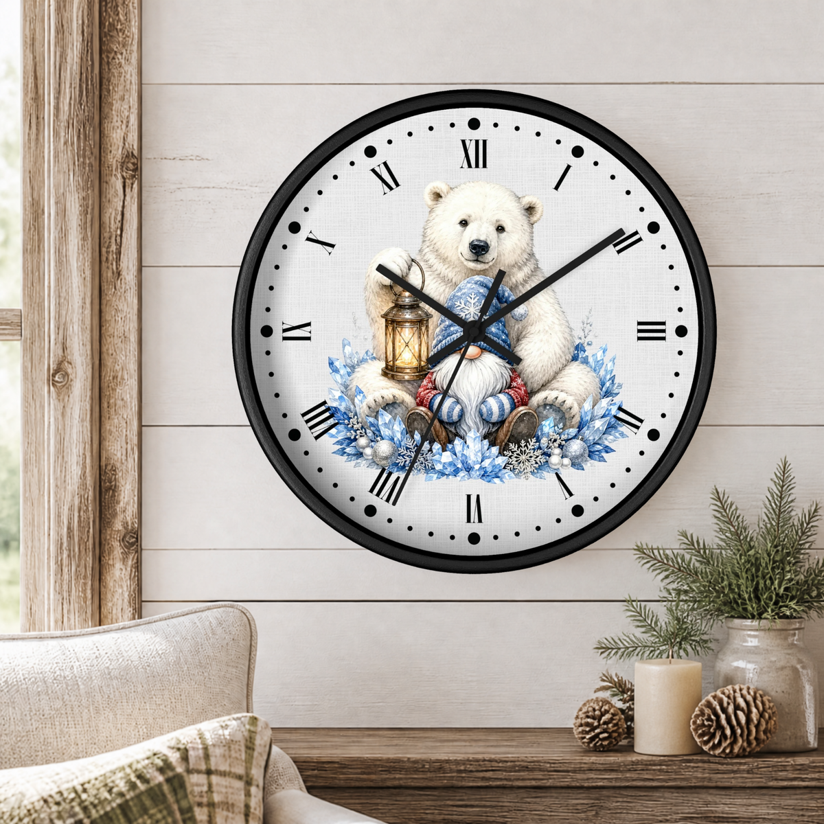 A round wall clock with a black frame and a white face featuring a polar bear illustration holding a lantern and blue winter flowers, mounted on a light wood paneled wall above a wooden table with candles and greenery.