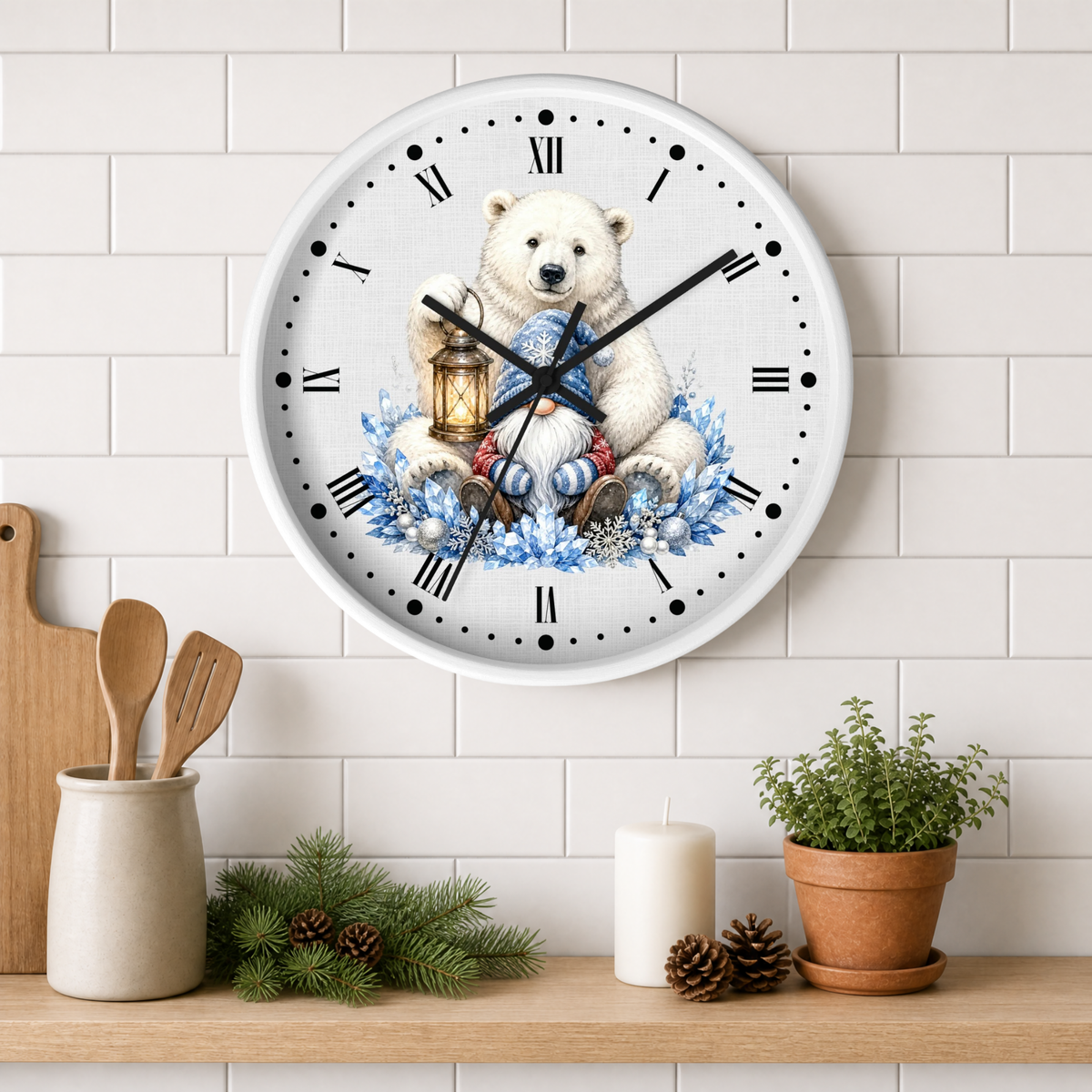 A round wall clock with a white face and black Roman numerals, featuring a printed illustration of a polar bear holding a lantern above blue floral elements. The clock is mounted on a white subway tile wall above a wooden shelf styled with kitchen utensils, pine branches, a candle, and a potted plant.