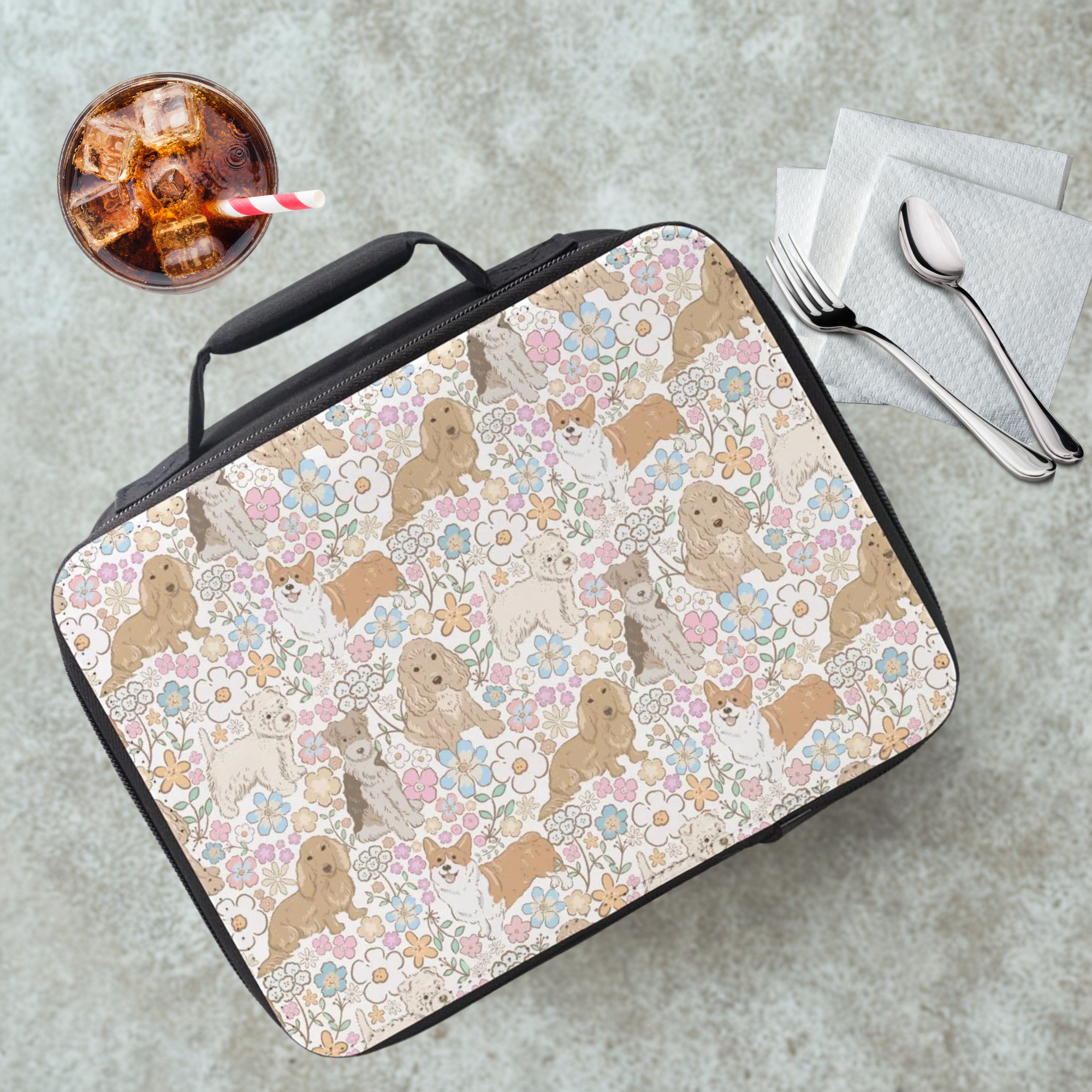 Insulated lunch bag with dogs and floral pattern on a cafeteria table with a drink and utensils.