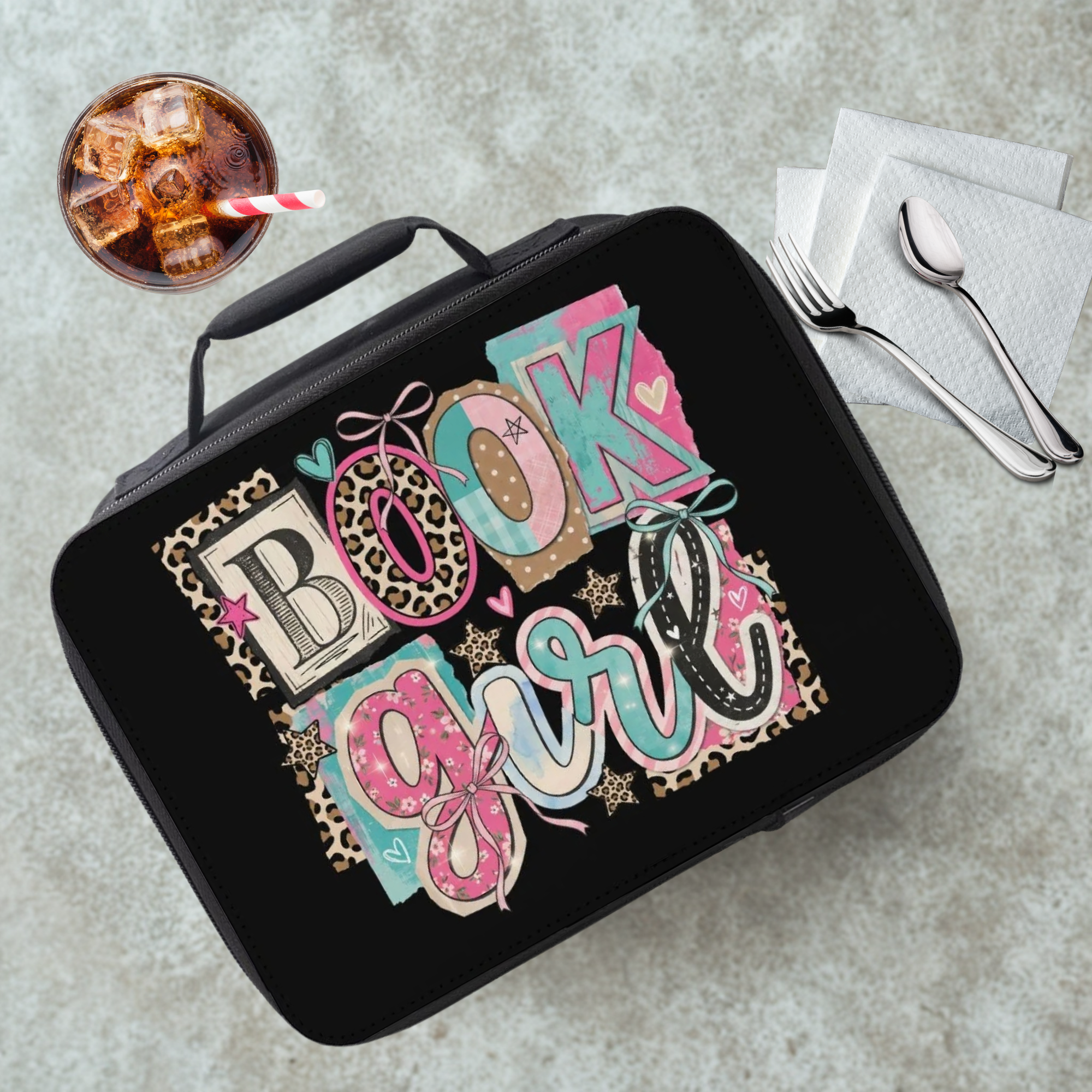 Black lunch bag with a colorful 'Book Girl' design on a gray table with a drink and utensils.
