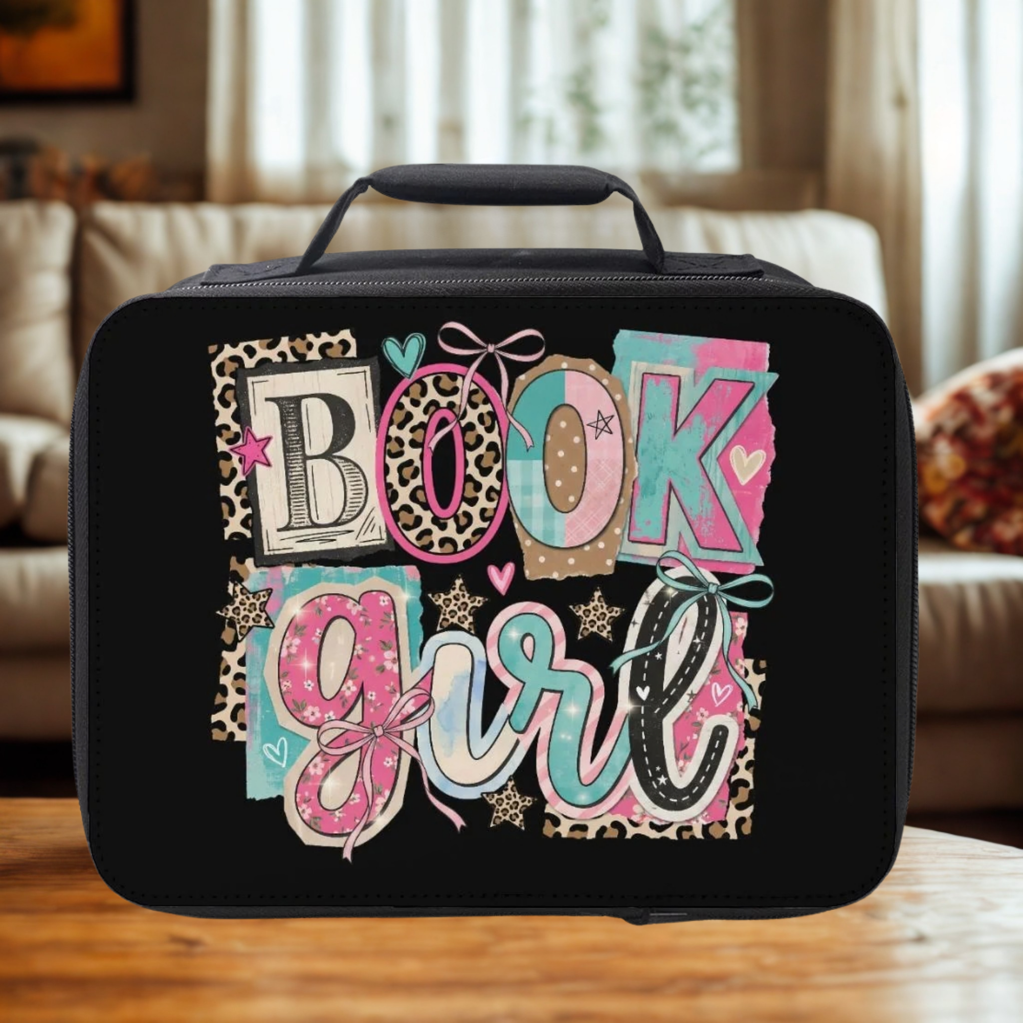 Black lunch bag with 'BOOK girl' text design on a wooden coffee table in a cozy living room.