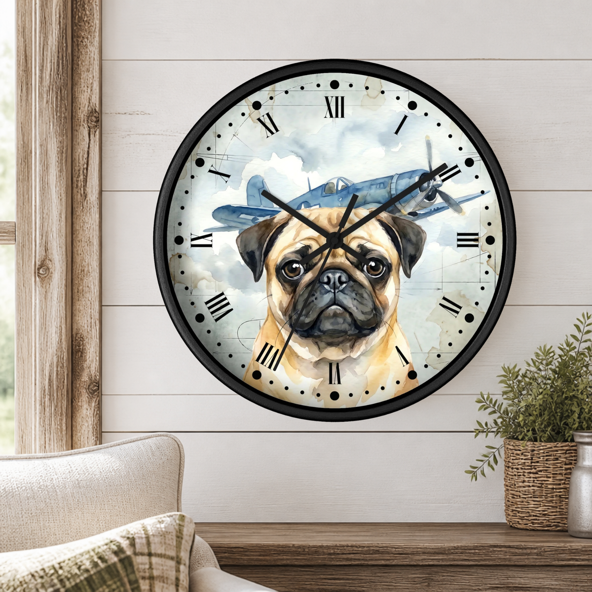 A round wall clock with a black frame and Roman numerals, featuring a watercolor-style illustration of a pug dog with a vintage blue airplane behind it. The clock is mounted on a white shiplap wall above a wooden console table with a small potted plant.