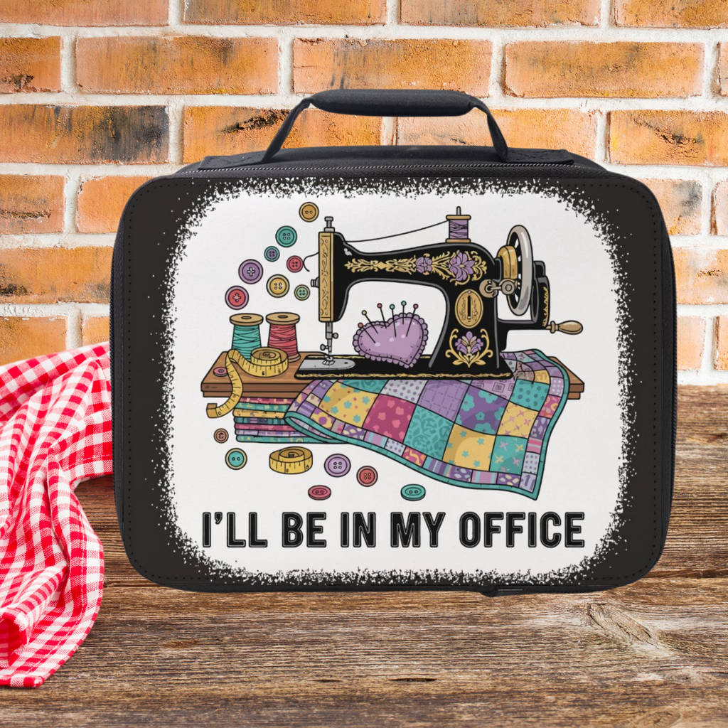 Black insulated lunch bag with sewing machine design and text 'I'll be in my office' on a wooden picnic table.