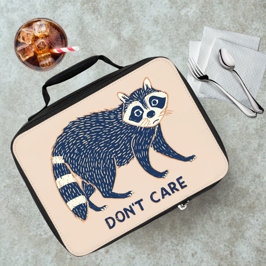 Lunch bag with raccoon design and 'Don't Care' text on a cafeteria table with a drink and utensils.