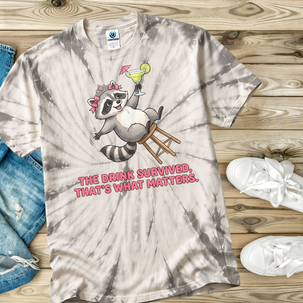 Tie-dye t-shirt in the color Spider Silver with a raccoon graphic and text on a wooden surface.