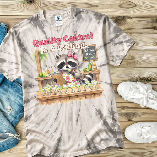 Tie-dye t-shirt with a raccoon character and 'Quality Control is a Calling' text on a wooden surface.