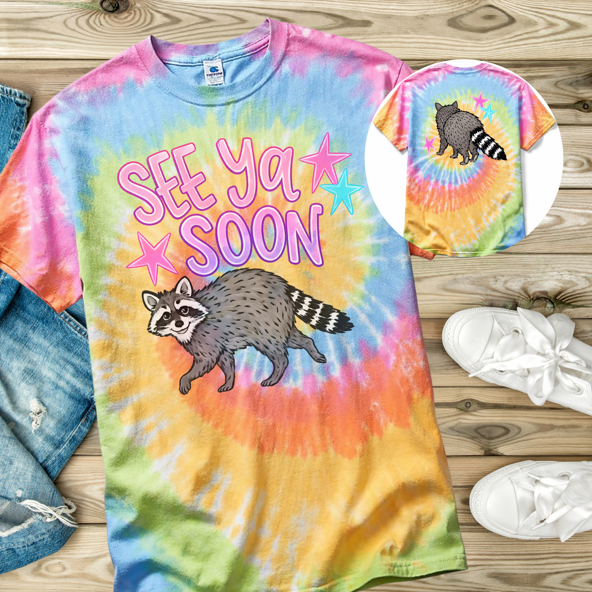 Colorful tie-dye t-shirt with hand drawn raccoon design and 'See Ya Soon' text on a wooden surface.