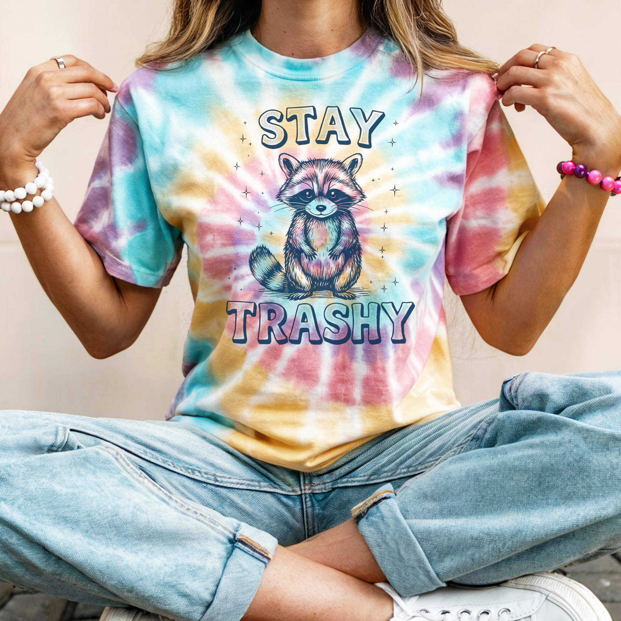 Person wearing a tie-dye t-shirt with a raccoon graphic and 'Stay Trashy' text.