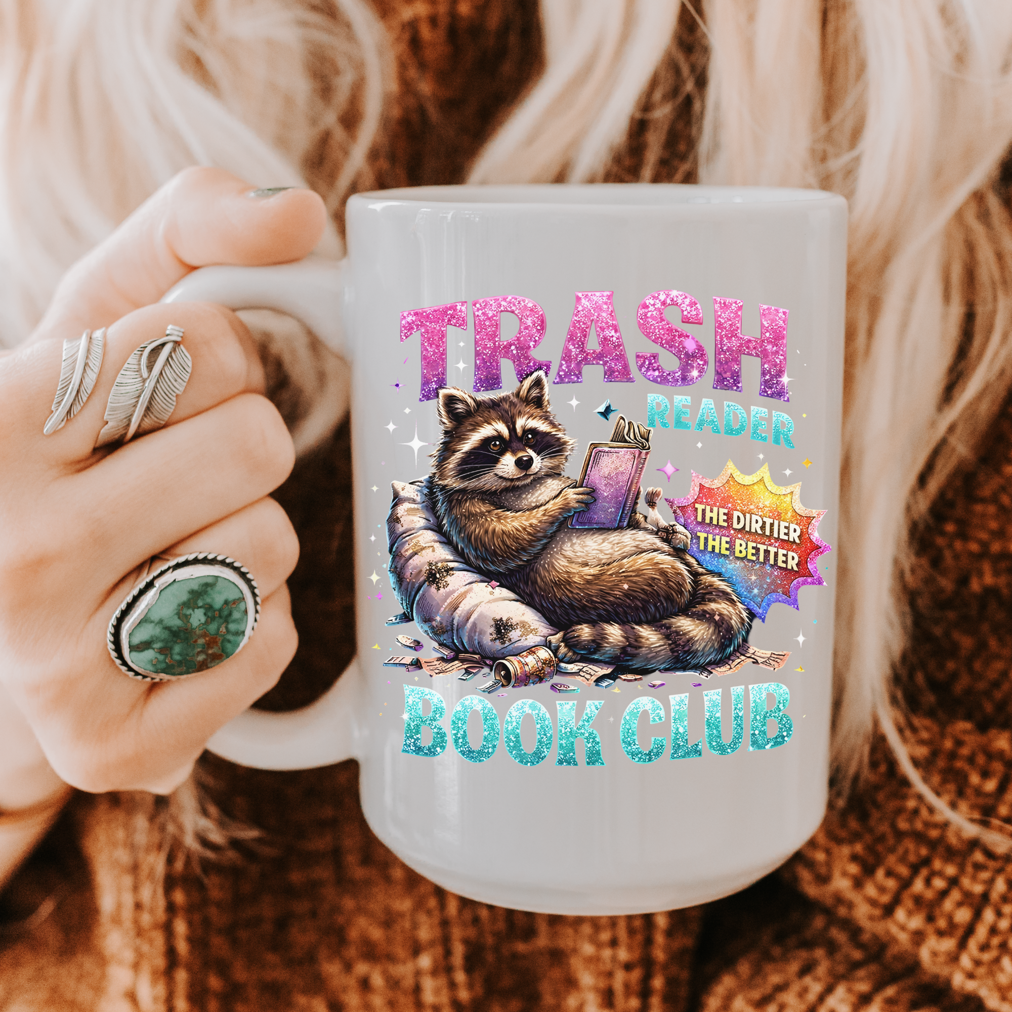 Mug with a raccoon graphic and text 'Trash Reader, The Dirtier The Better Book Club' held by a person.