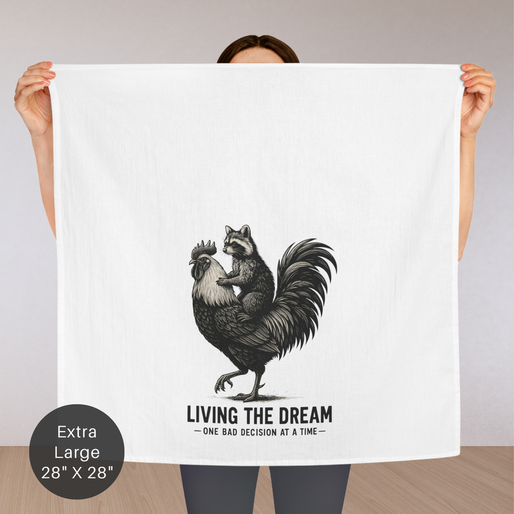 Person holding an extra large tea towel with a graphic of a raccoon riding a rooster, text 'Living the Dream' and 'One bad decision at a time', on a plain background.