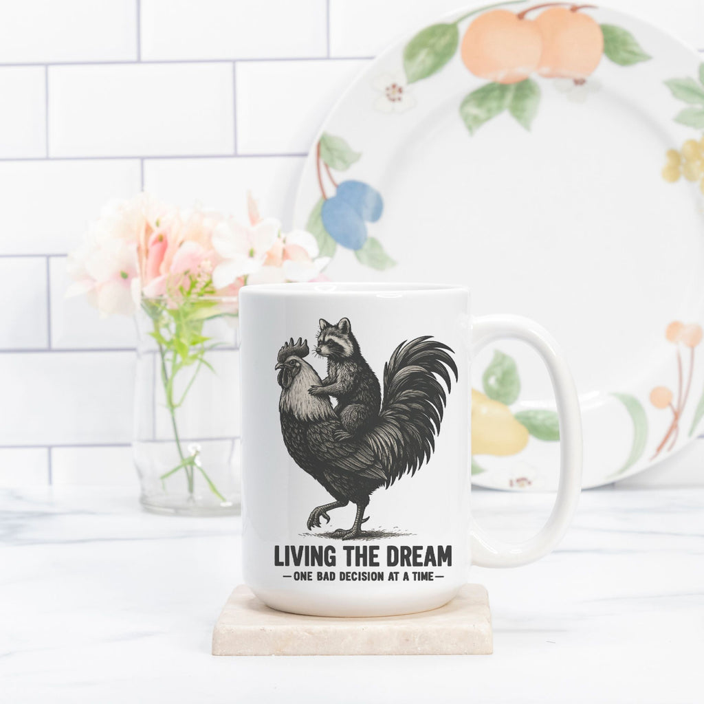 Mug with rooster and raccoon design and text 'Living the Dream' on a white surface with a floral plate in the background.