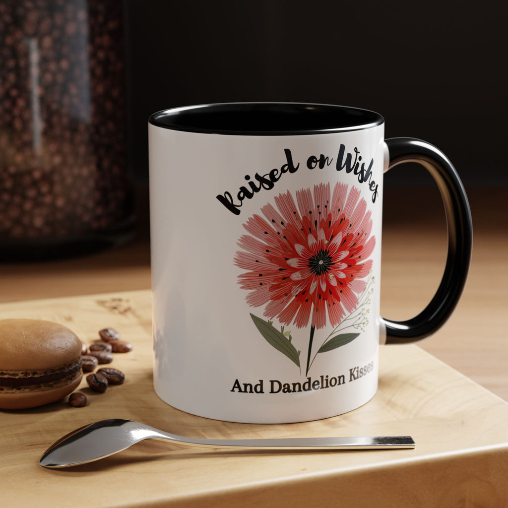White mug with black interior and handle, featuring a red flower design and text, on a wooden surface with coffee beans and a spoon.