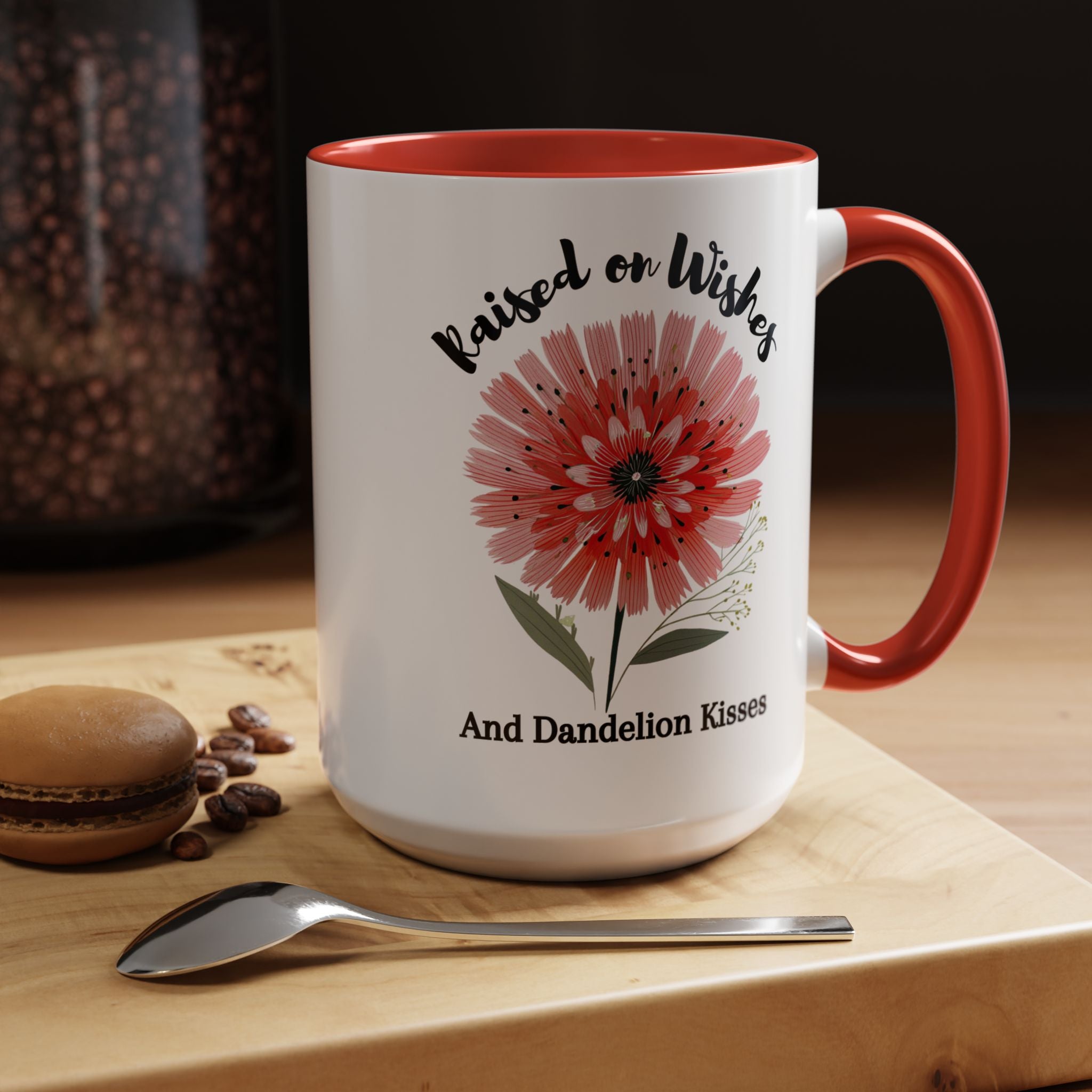 Red accent mug with floral design and text on a wooden surface with coffee beans and a spoon.