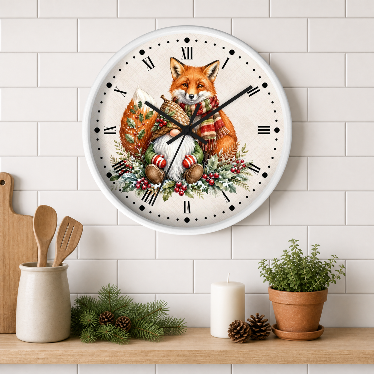 A round wall clock with a white frame and a festive illustration of a red fox wearing a striped scarf, surrounded by holiday greenery and ornaments. The clock is mounted on a white subway tile wall above a wooden shelf styled with kitchen utensils, a candle, pinecones, and a potted plant.