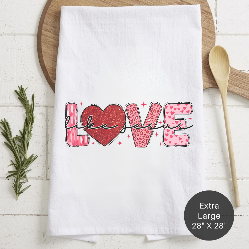 White tea towel with 'LOVE Like Jesus' text and heart design on a wooden surface