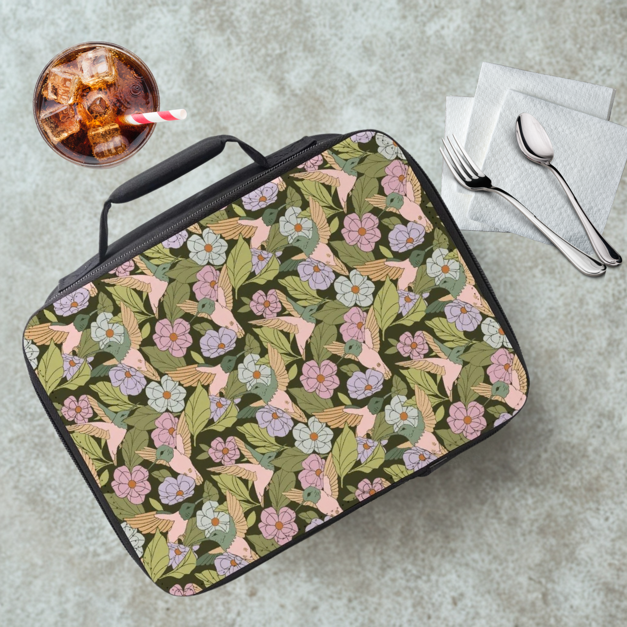 Floral and hummingbird patterned lunch bag on a cafeteria table with a drink and utensils.