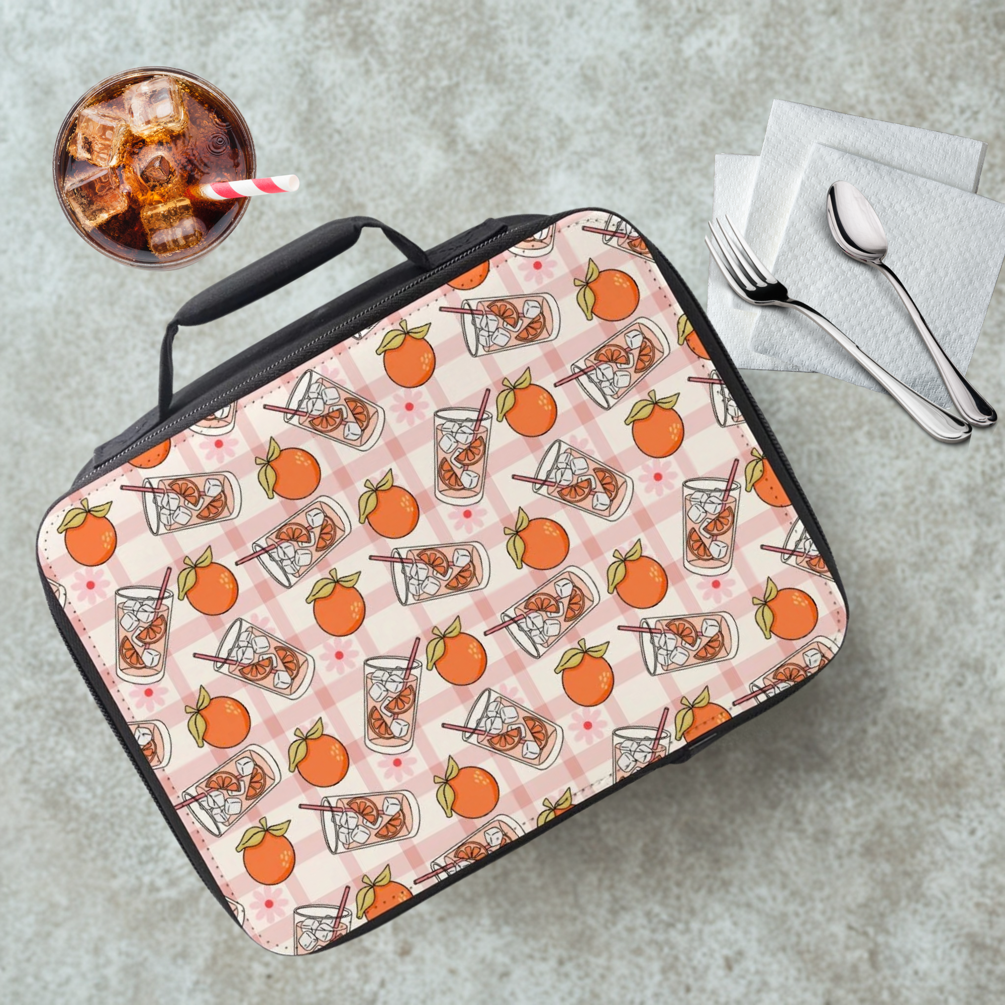 Lunch bag with orange and juice pattern on a cafeteria table with a drink and utensils.