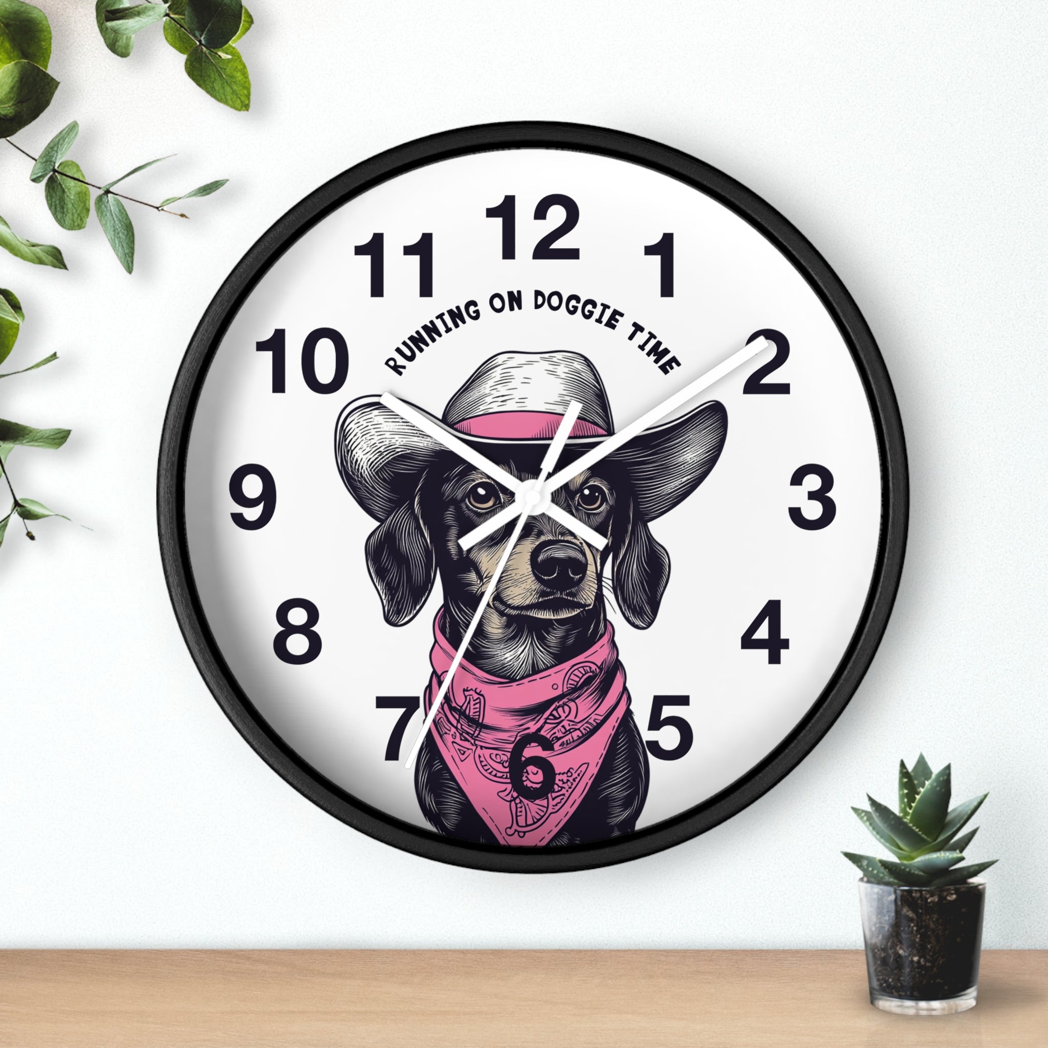 Black Wall clock with white hands and  a dog illustration and 'Running on Doggie Time' text, placed on a surface with plants.