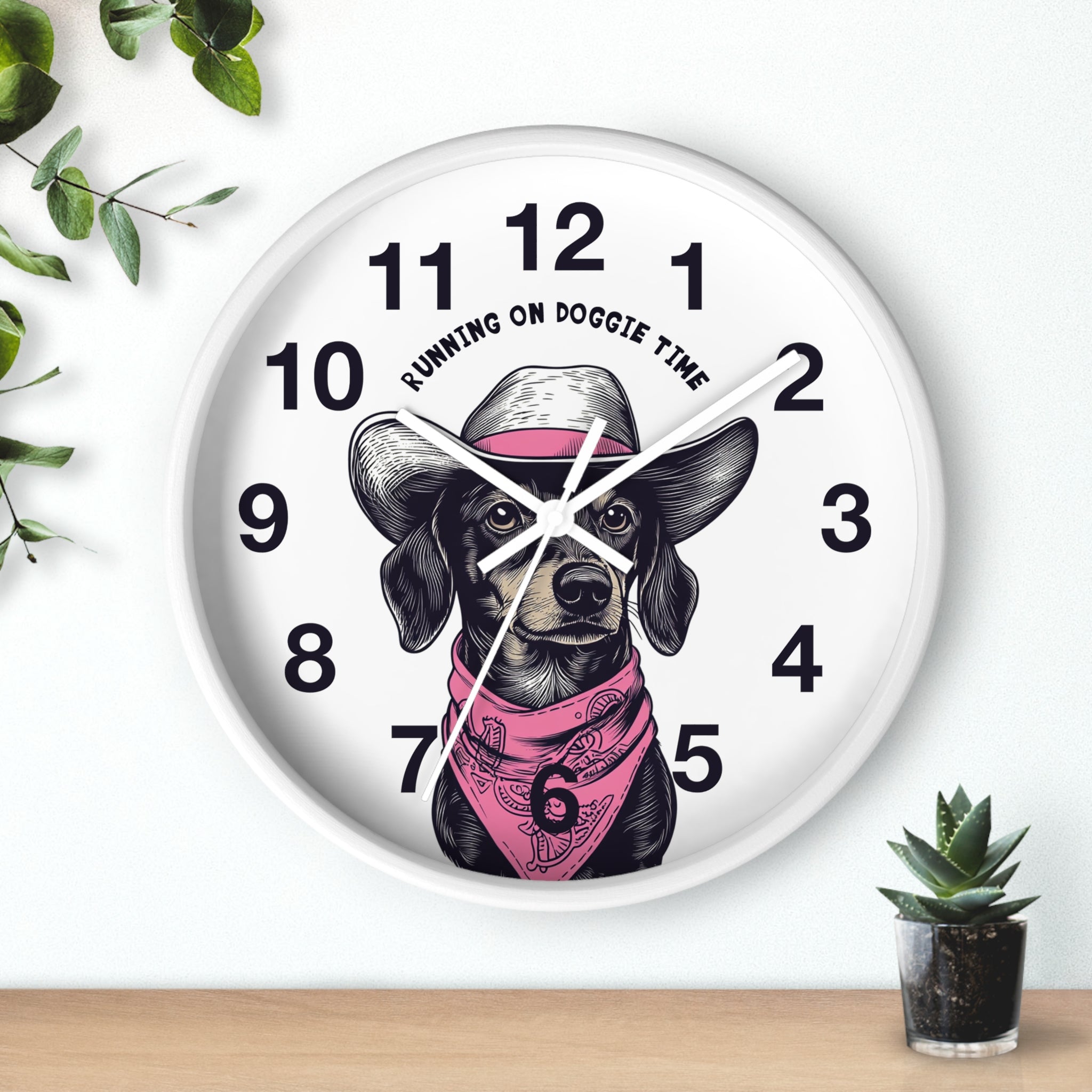 White wall clock with white hands and a dog design and 'Running on Doggie Time' text, placed on a surface with plants.