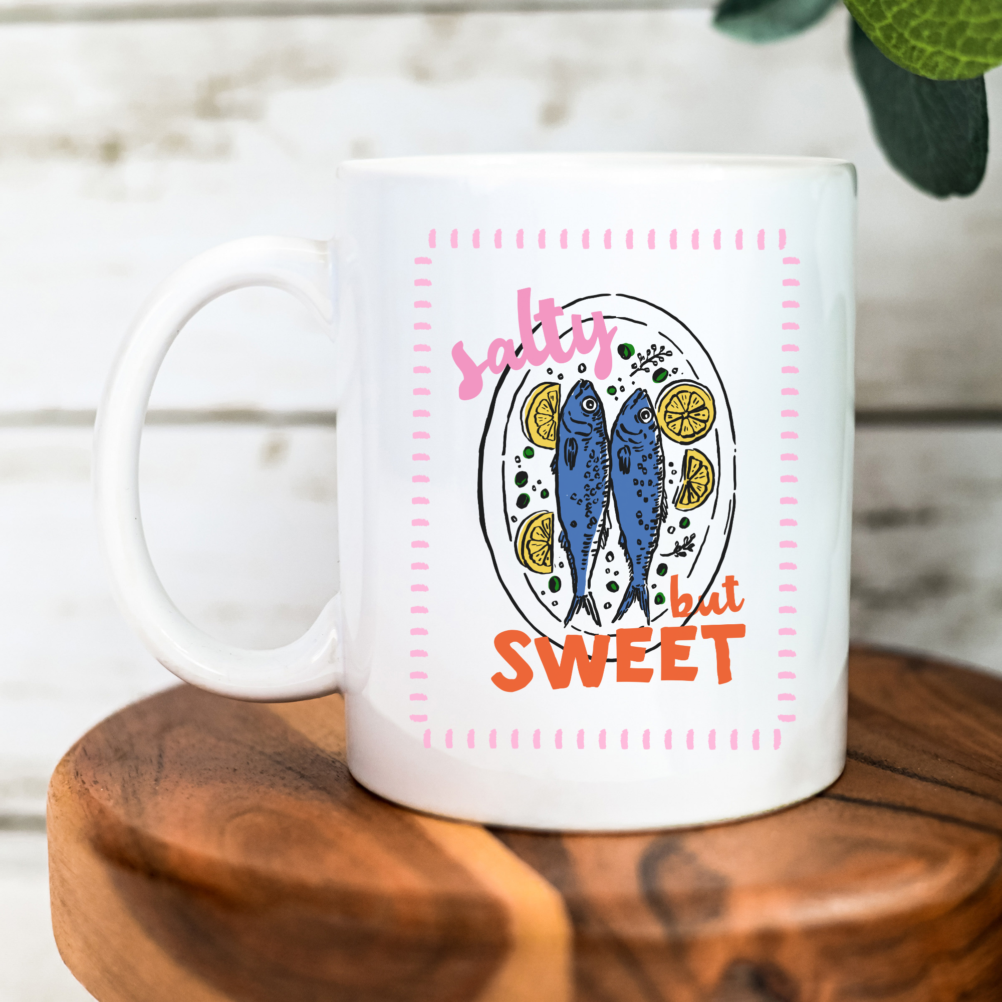 White 11oz. mug with sardine fish design and text 'salty but sweet' on a wooden surface.
