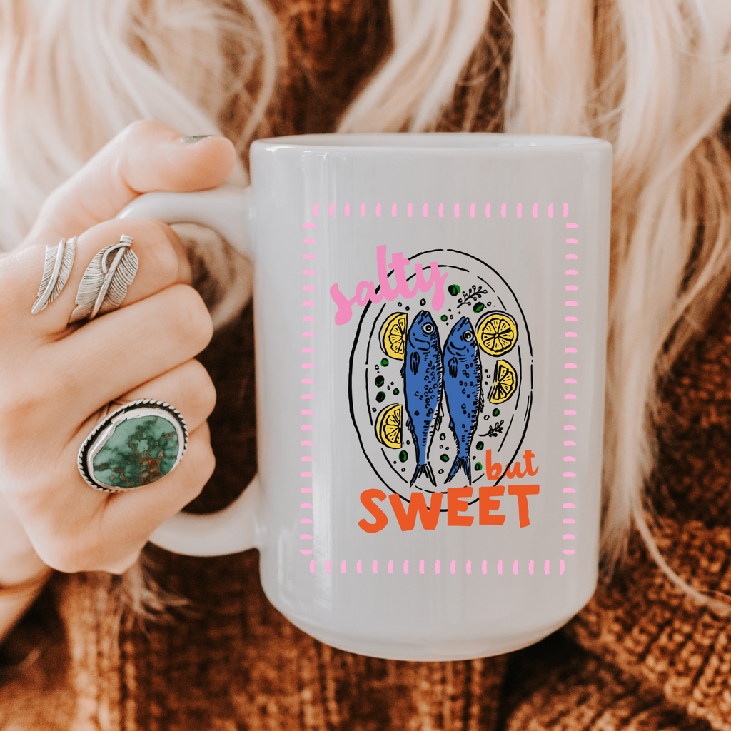 Person holding a 15oz. mug with a sardine fish design and text on a textured surface