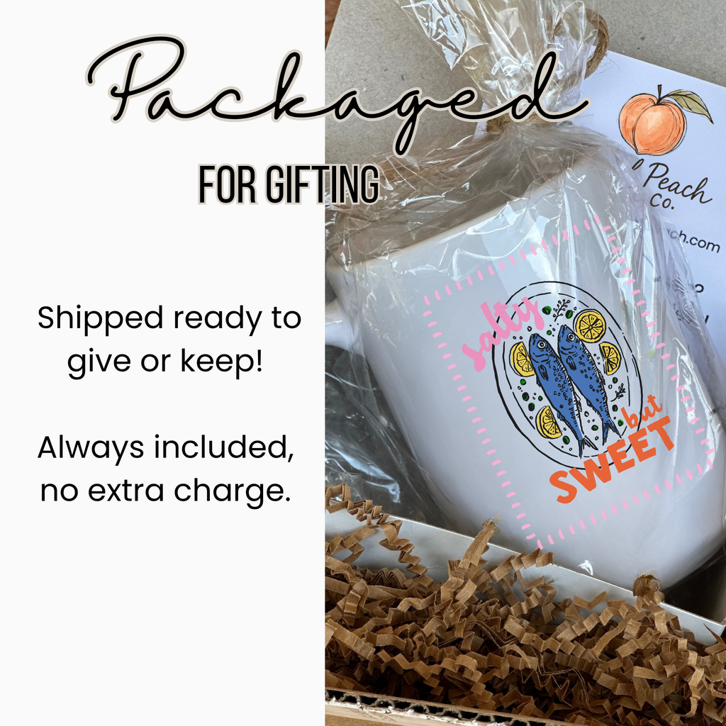 White 15oz. mug with a sardine fish design and text, wrapped in clear plastic inside a white gift box with brown paper underneath, labeled 'Packaged For Gifting'