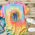 Colorful tie-dye t-shirt with fish design and text on a wooden surface with jeans and shoes.