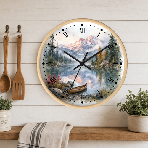 Round wall clock with a light wood frame featuring a scenic mountain lake landscape print, hanging on a white wood plank wall above a shelf with plants and kitchen utensils.