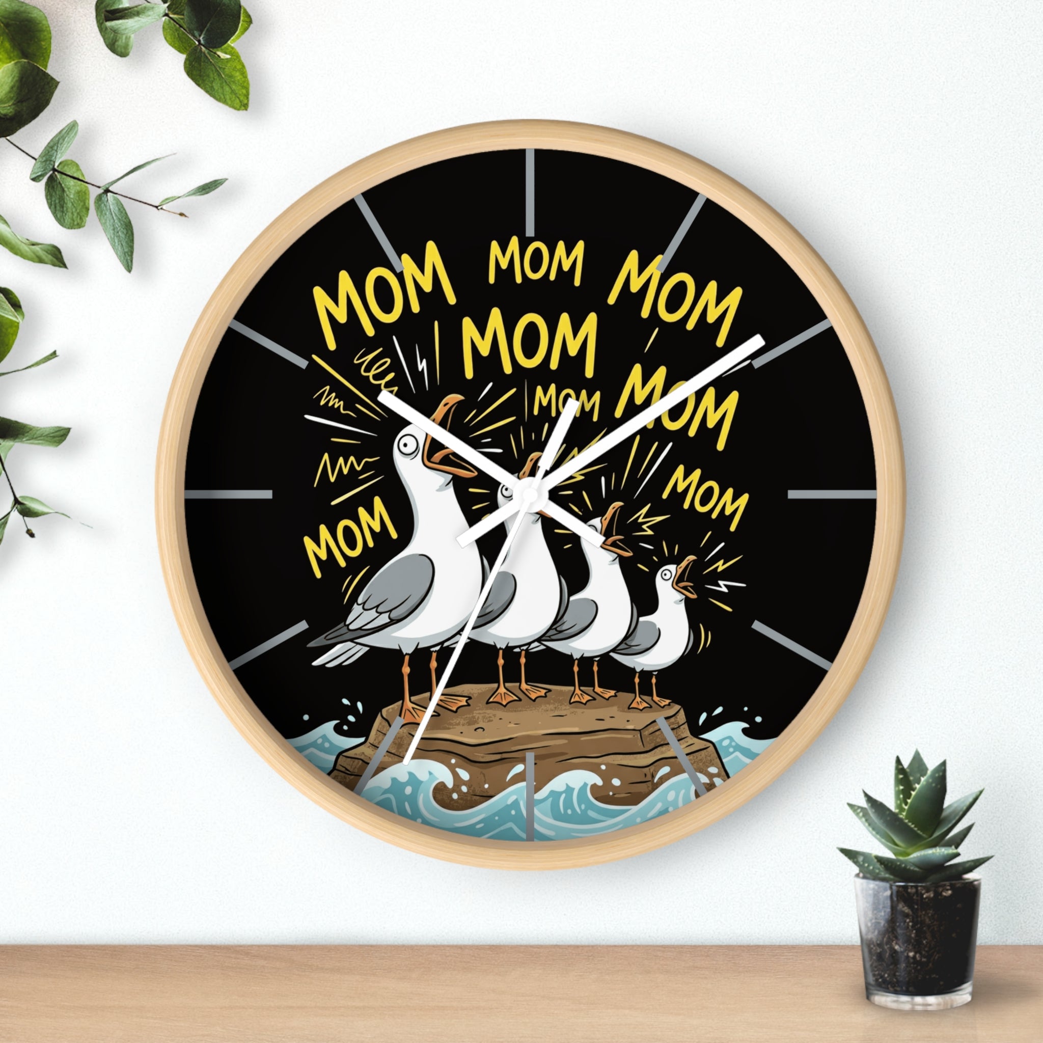Round wood wall clock with seagulls and 'Mom' text on a black background, placed on a wooden surface with a plant.