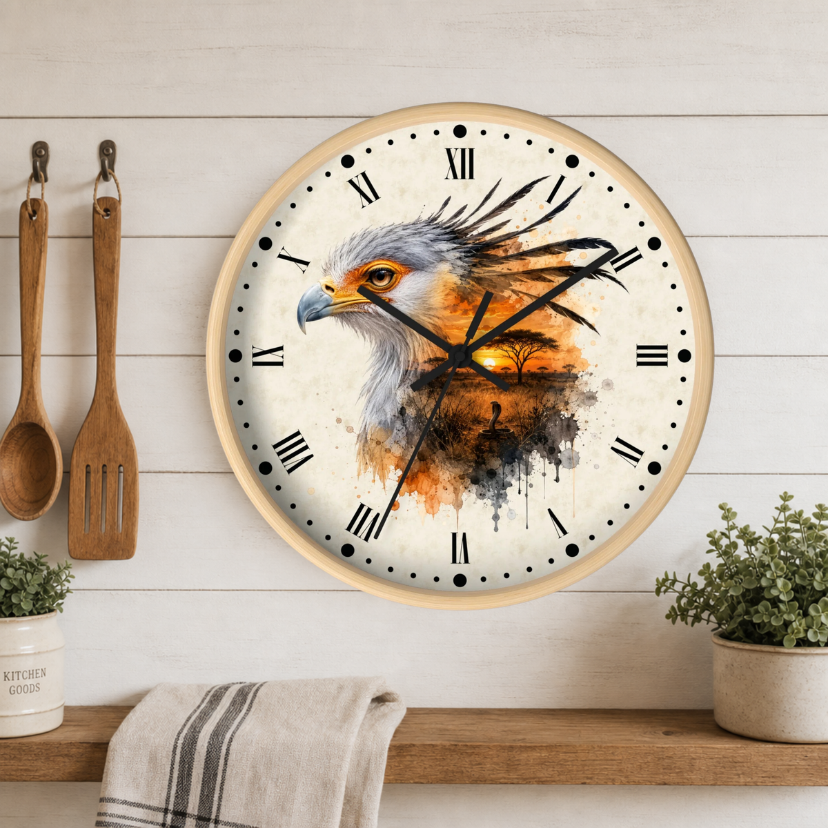 A round wall clock with a light wood frame hangs on a white wood-paneled wall above a wooden shelf. The clock face features a watercolor-style illustration of an eagle's head over an orange and brown sunset landscape.