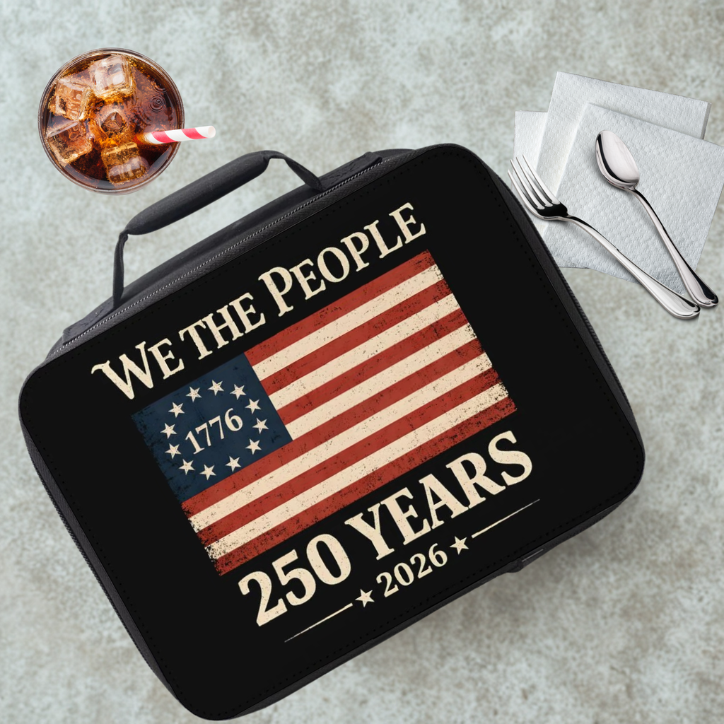 Black lunch box with 'We the People' and American flag design on a cafeteria table with a drink and utensils.