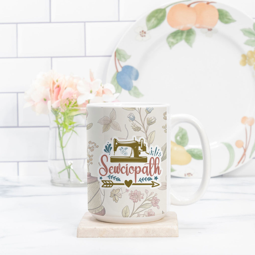 Mug with 'Sewciopath' design on a white surface with a decorative plate in the background.
