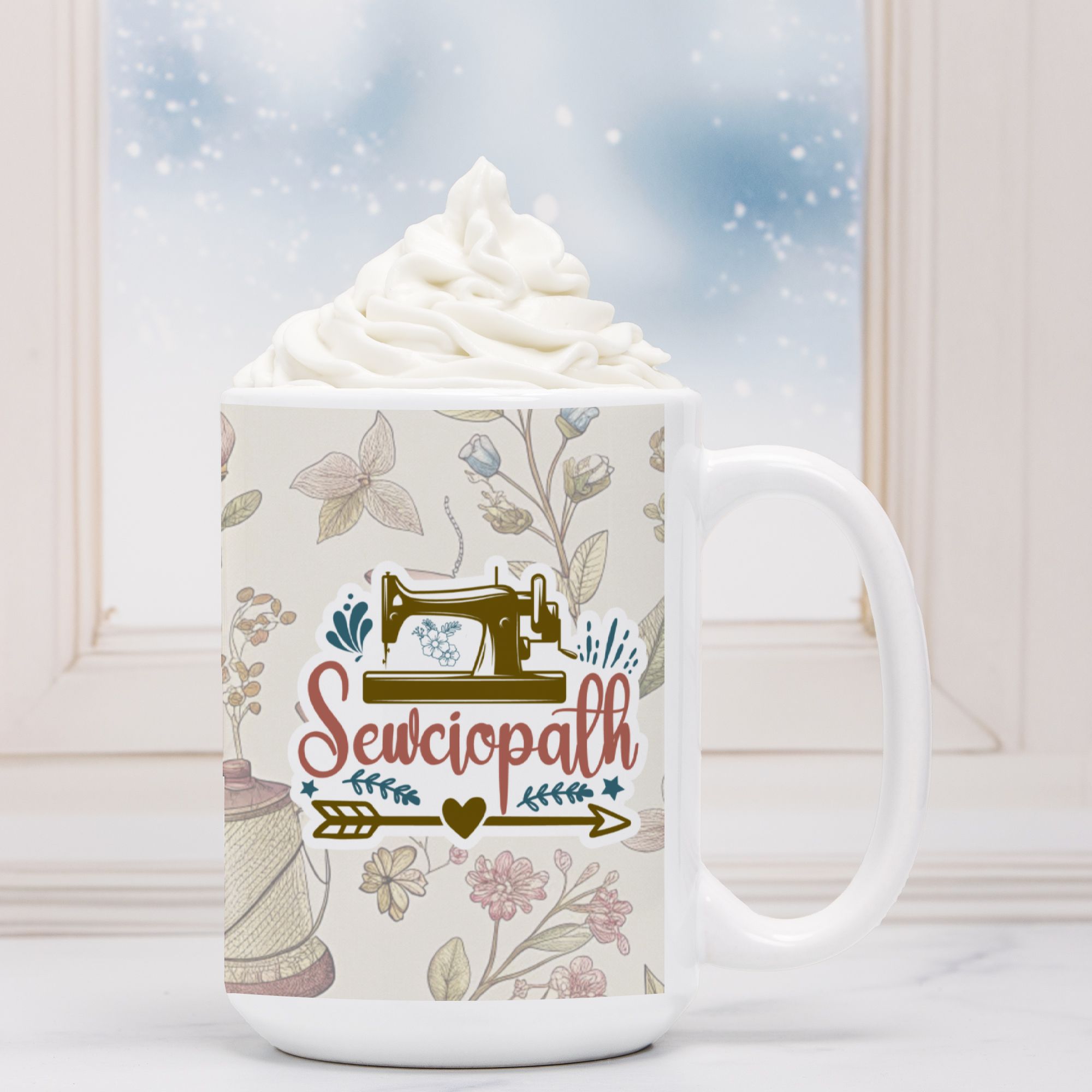 White mug with sewing-themed design and 'Sewciopath' text, filled with hot chocolate and whipped cream.