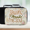 Insulated lunch bag with 'Sewing Mends The Soul' sticker style text and floral sewing themed pattern on a blurred background