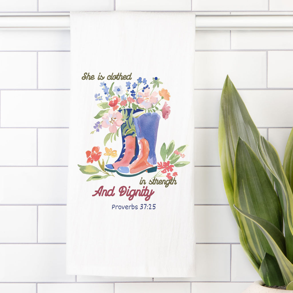 Decorative tea towel with floral design and text on a white tiled wall.