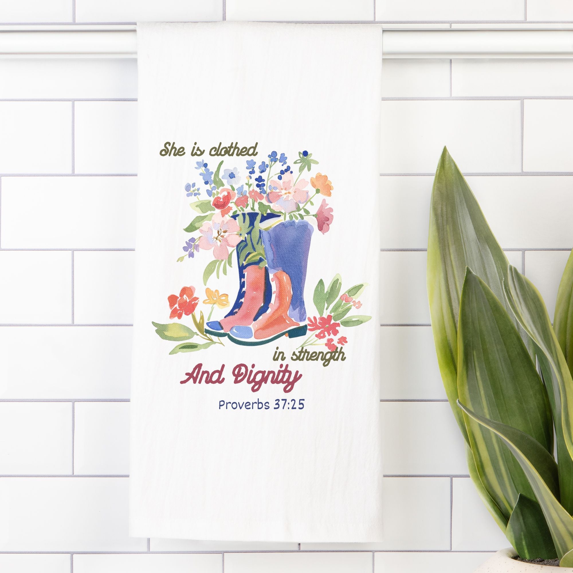 Decorative tea towel with floral design and text on a white tiled wall.