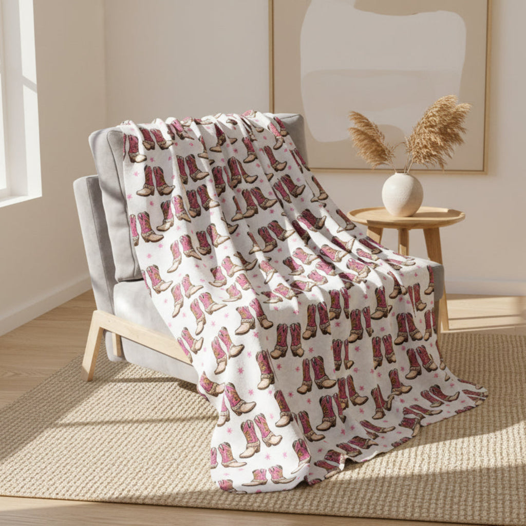 Blanket with pink cowboy boot pattern draped over a chair on a light gray background