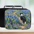 Black lunch bag with a design of a Shetland sheep dog walking through flowers on a white surface.