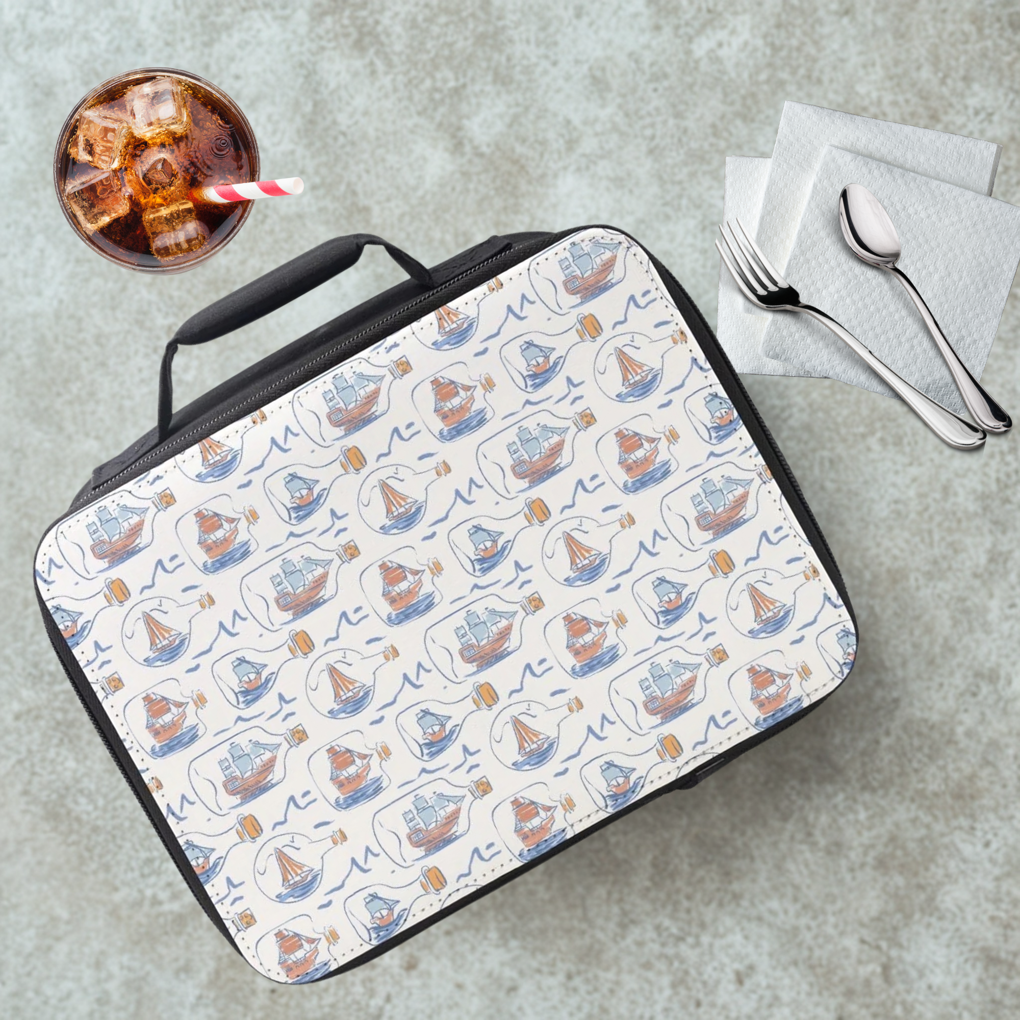 Lunch bag with boat pattern on a cafeteria table with a drink and utensils.