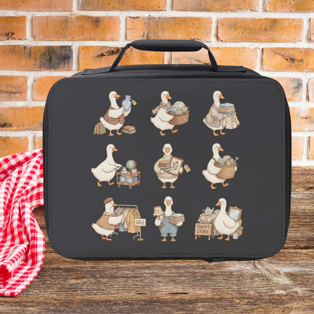 Black lunch bag with cartoon thrift shopping geese illustrations on a wooden picnic table and brick wall background