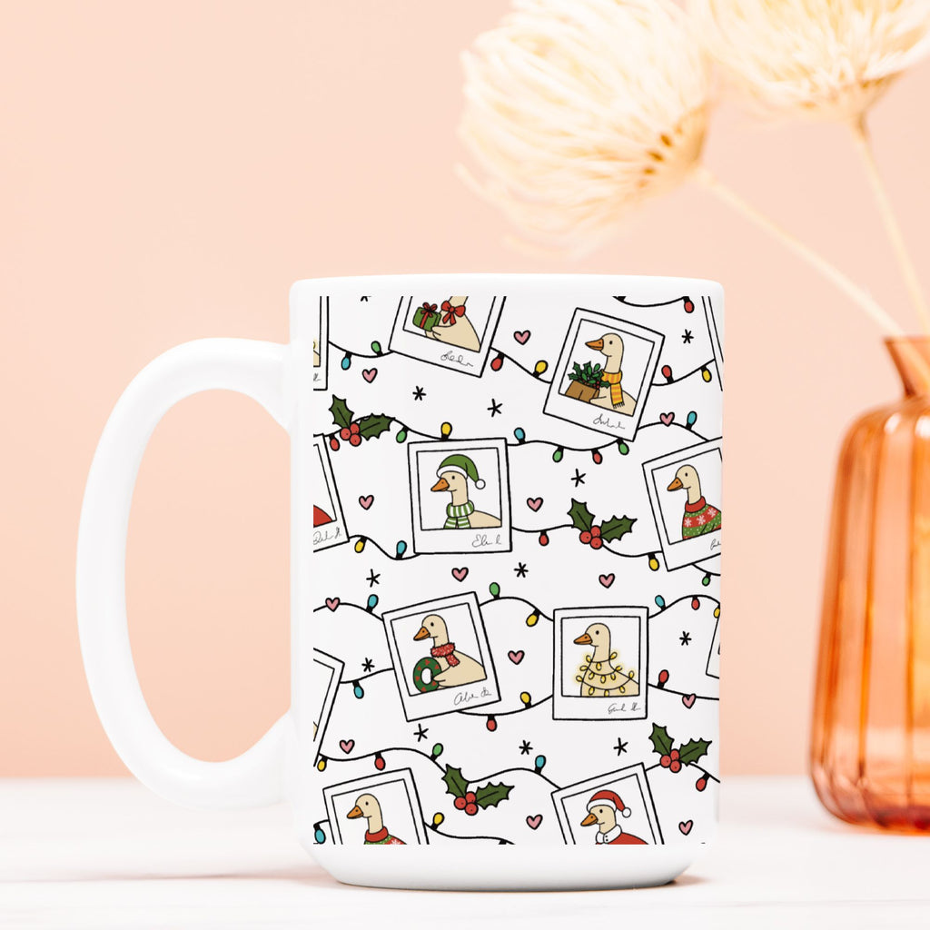 White mug with Christmas-themed design featuring geese, lights, and holly on a light pink background.