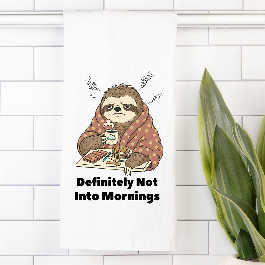 Tea towel with a Cartoon sloth in a blanket with coffee and toast, text 'Definitely Not Into Mornings', on a white tiled wall.