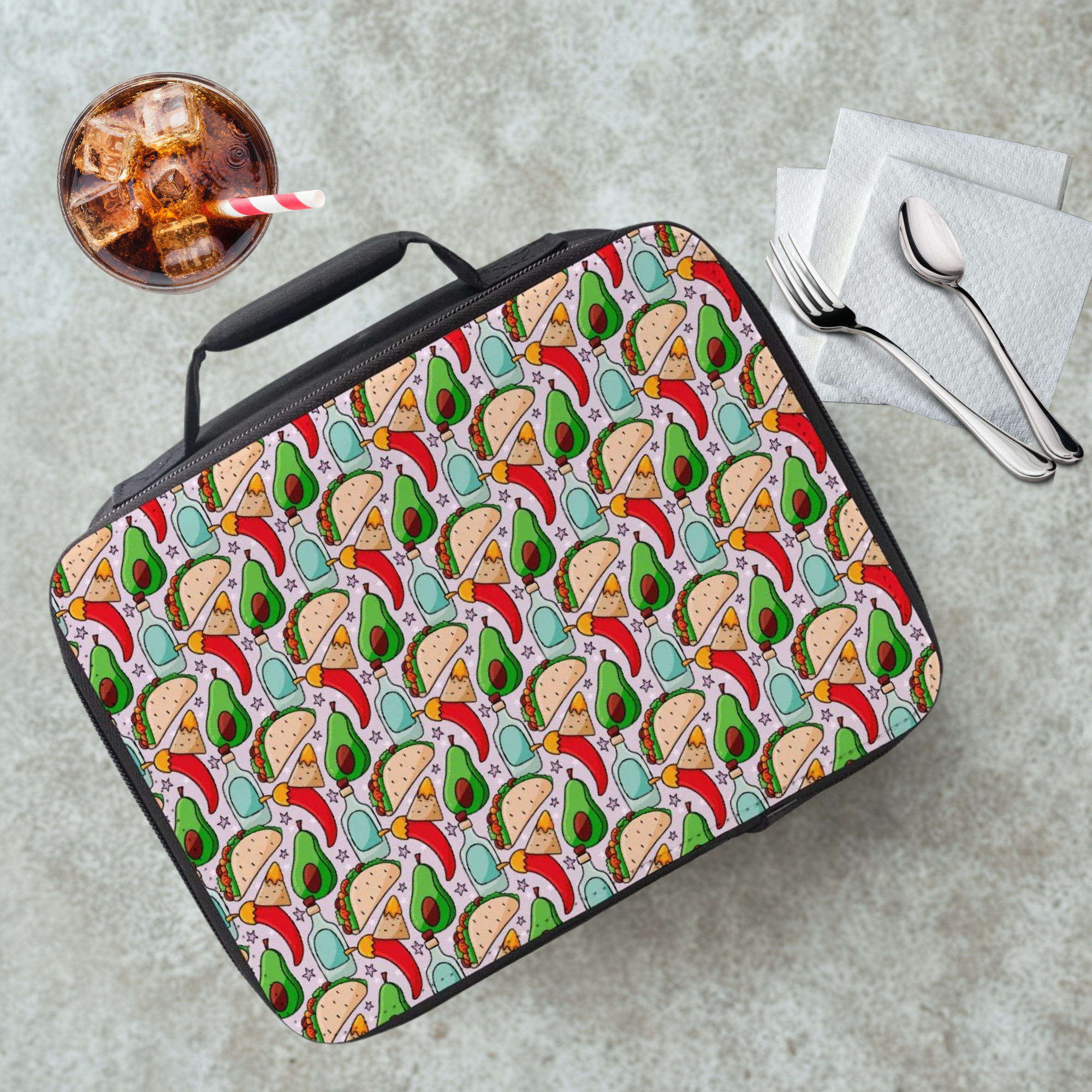 Lunch bag with avocado and taco pattern on a cafeteria table with a drink and utensils.