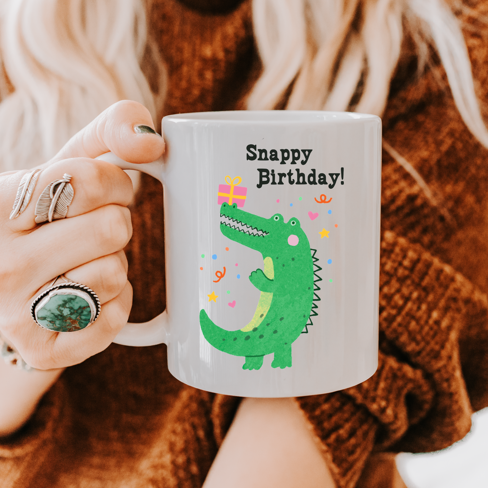 Person holding a mug with a crocodile graphic and 'Snappy Birthday!' text.