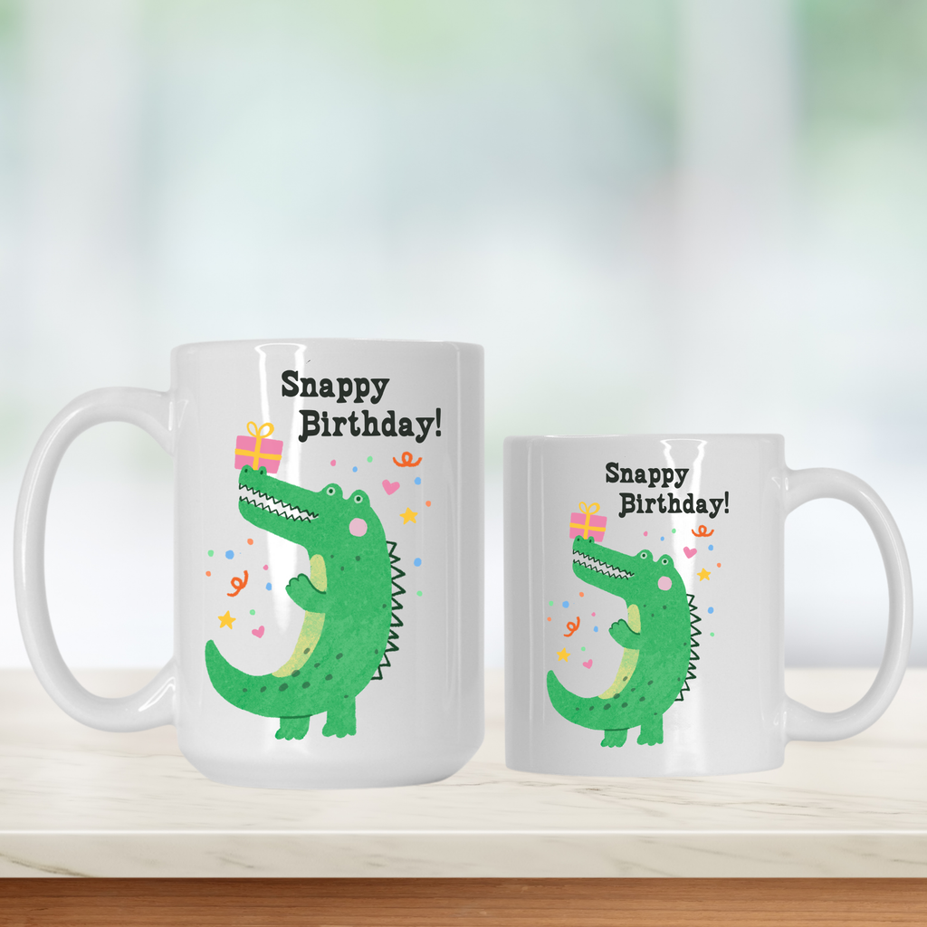 Two white mugs with a green alligator design and 'Snappy Birthday!' text on a light background.