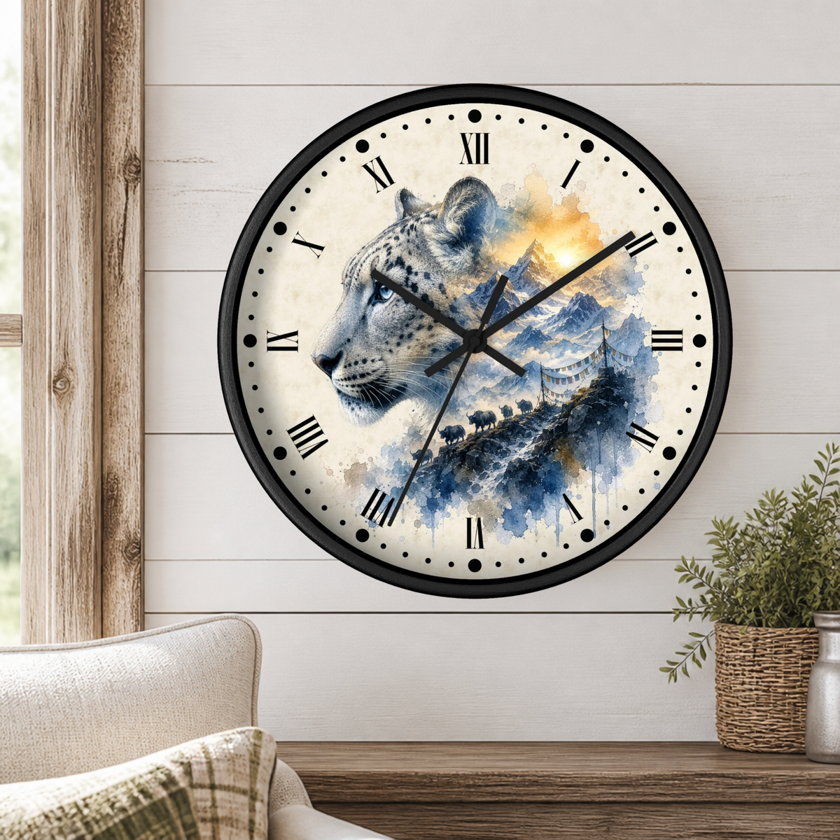 A round wall clock with a black frame and a watercolor-style leopard print face, mounted on a white wood-paneled wall above a wooden shelf with a plant and part of a sofa visible.