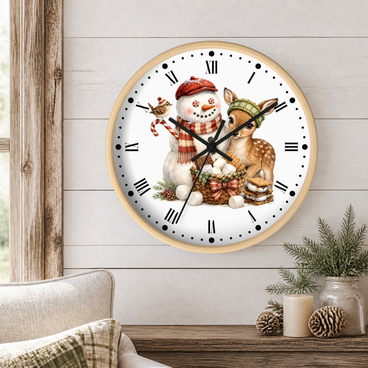 A round wall clock with a light wood frame hangs on a white shiplap wall above a wooden table. The clock face features a festive illustration of a snowman and a deer in winter clothing, with black Roman numerals and hands.