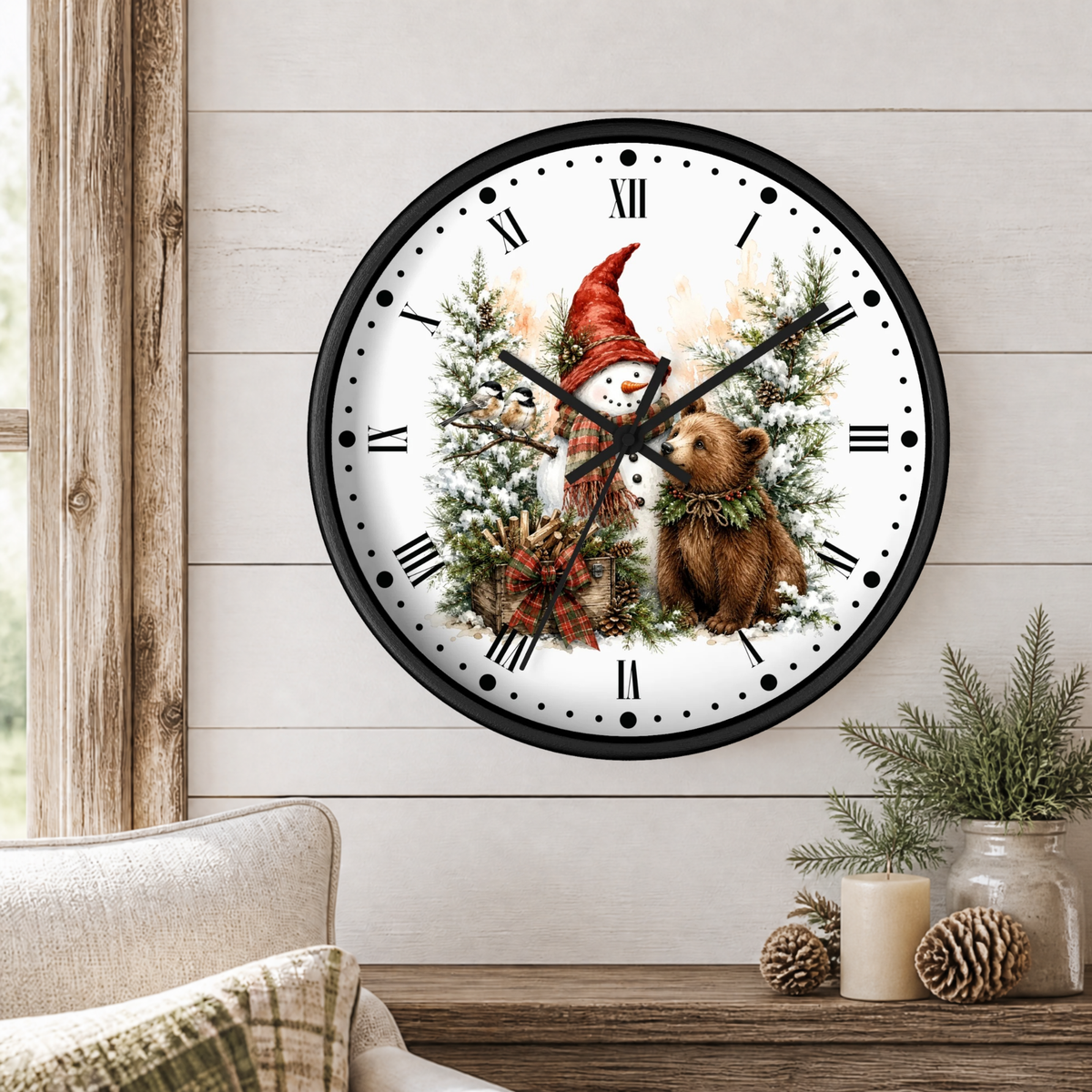 A round wall clock with a black frame and a winter woodland illustration of a snowman and bear on the face, hanging on a light wood paneled wall above a table with candles and pinecones.