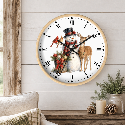A round wall clock with a light wood frame hangs on a white shiplap wall above a rustic wooden table. The clock face features a festive winter illustration of a snowman in a black top hat and red plaid scarf, standing next to a brown deer, with two red cardinals perched on a wreath decorated with red bows and green pine branches.